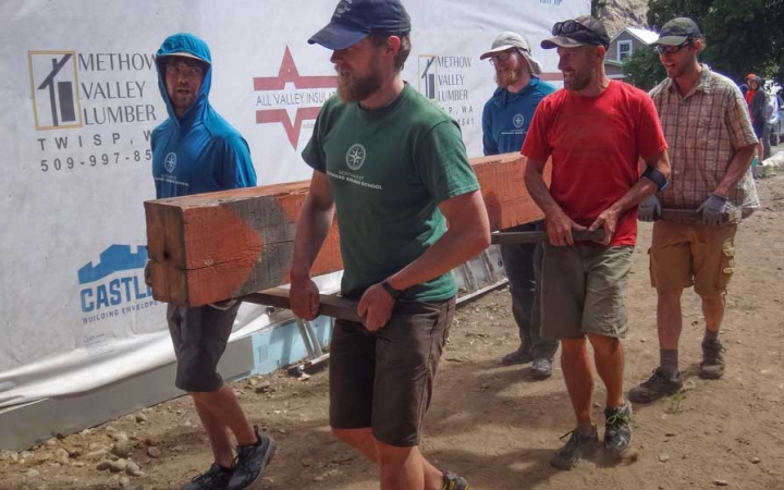 a group of veterans carry a large piece of wood during a service project